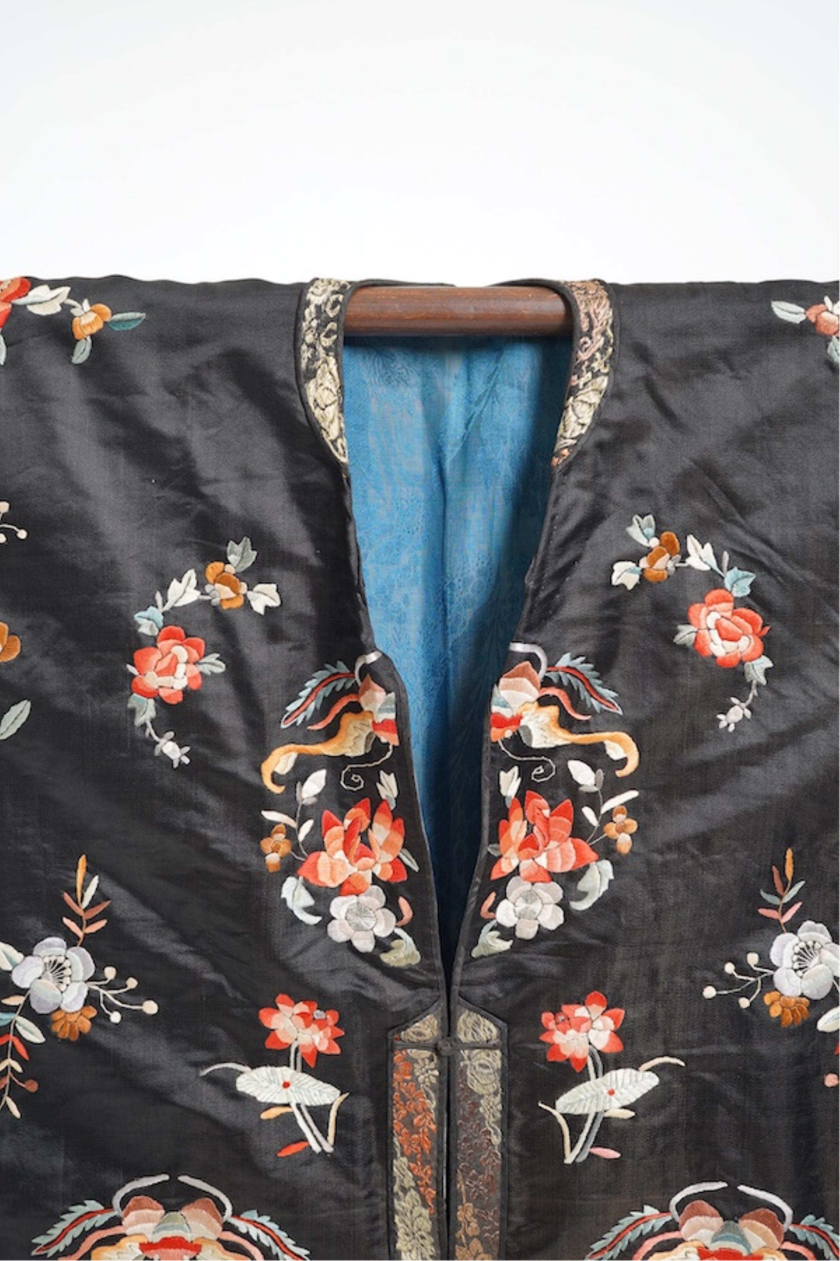 A late 19th early 20th century Chinese black silk polychrome embroidered ladies robe, decorated with cream silk, gilt and Peking knot bordered sleeve bands. The sleeve bands worked with fine figural and other embroidered